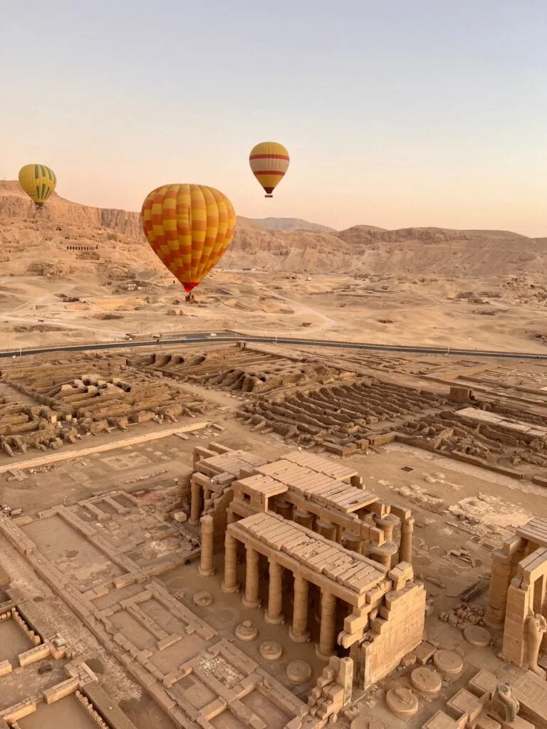 Hot-air balloons at dawn over the Luxor West Bank — drifting above Hatshepsut's Mortuary Temple, the Ramesseum, and the Valley of the Kings