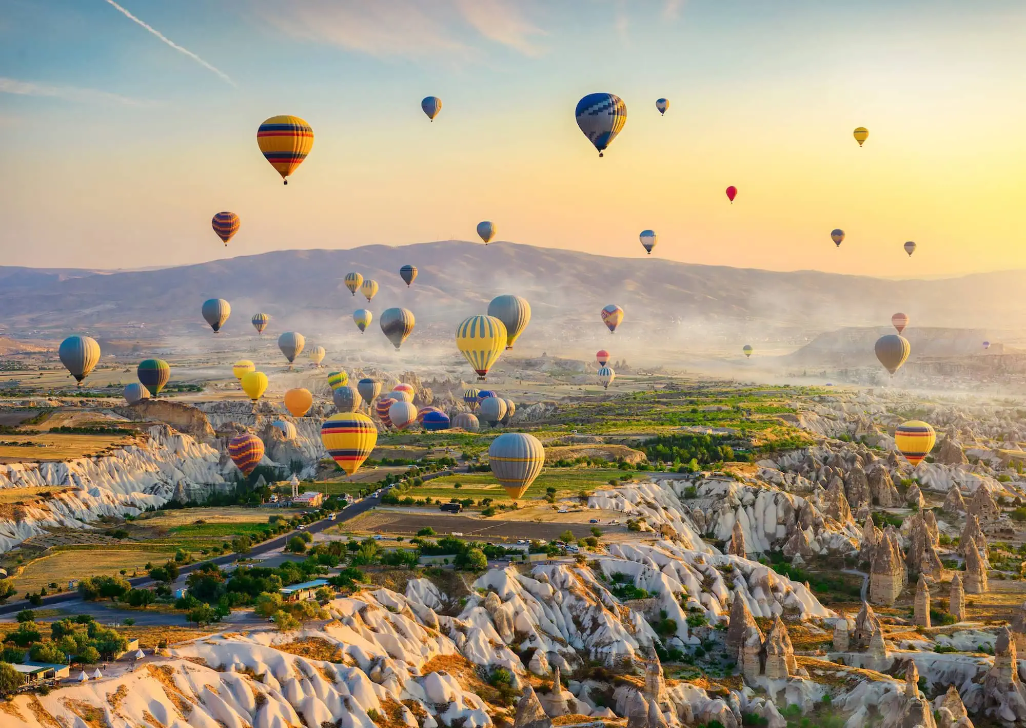 Hot-air balloons drifting over Cappadocia's fairy chimney rock formations at sunrise — Göreme valley, Turkey, one of the world's largest commercial hot-air-balloon operations