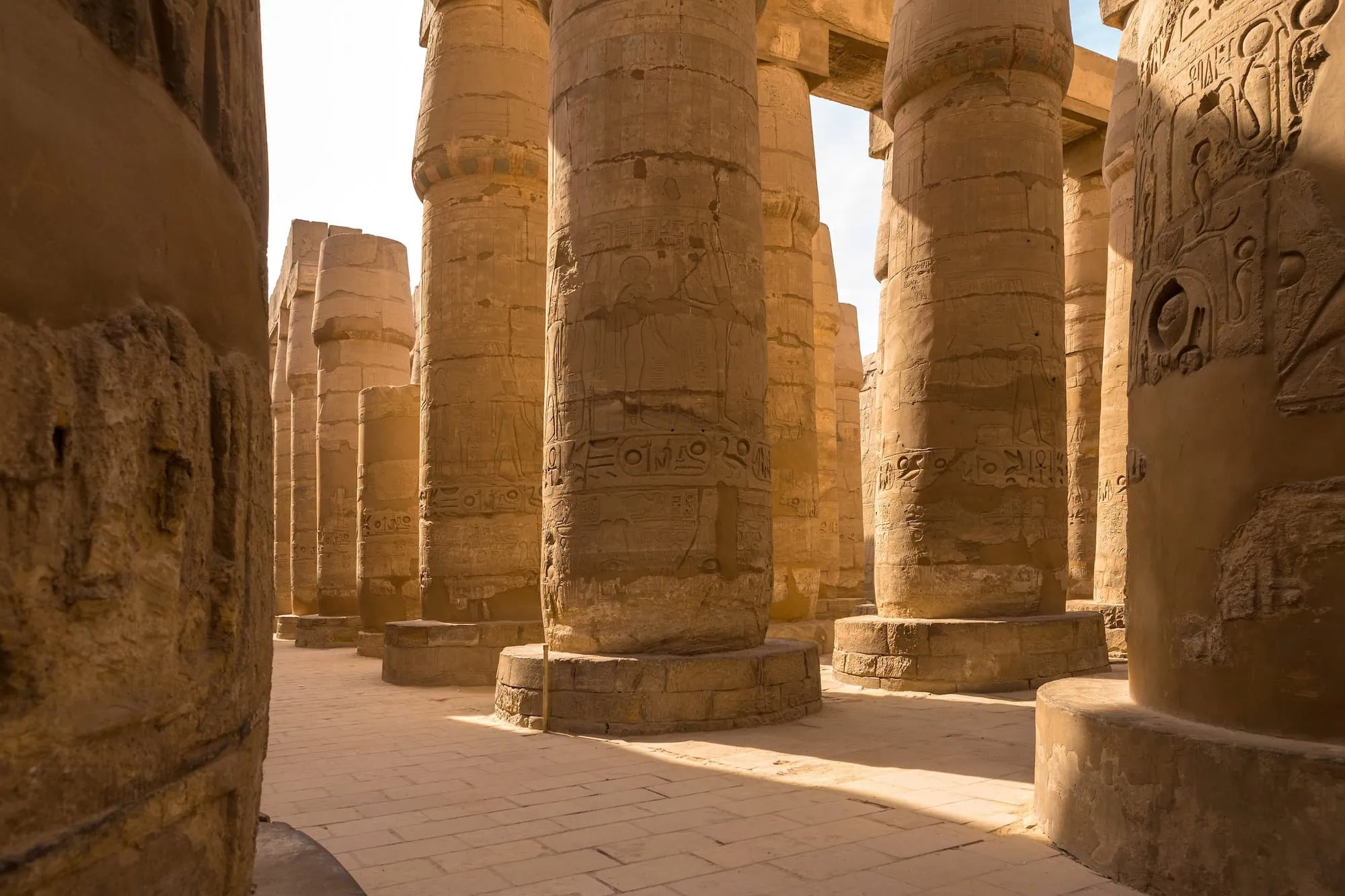 Rows of massive papyrus-form stone columns covered in hieroglyphic carvings inside the Great Hypostyle Hall at Karnak Temple, Luxor