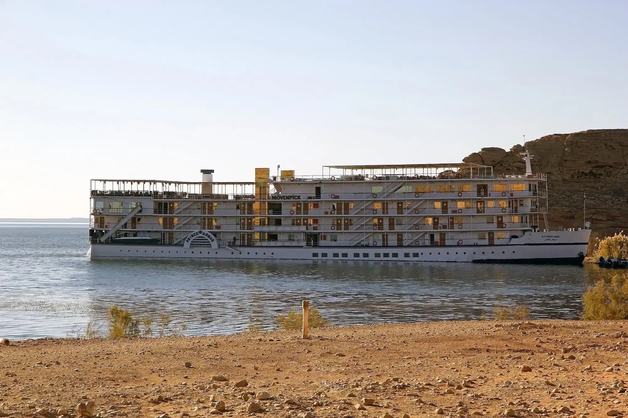 A luxury Lake Nasser cruise vessel moored on the calm blue lake with desert shoreline, the Nubian extension featured on longer luxury Egypt all-inclusive itineraries toward Abu Simbel.