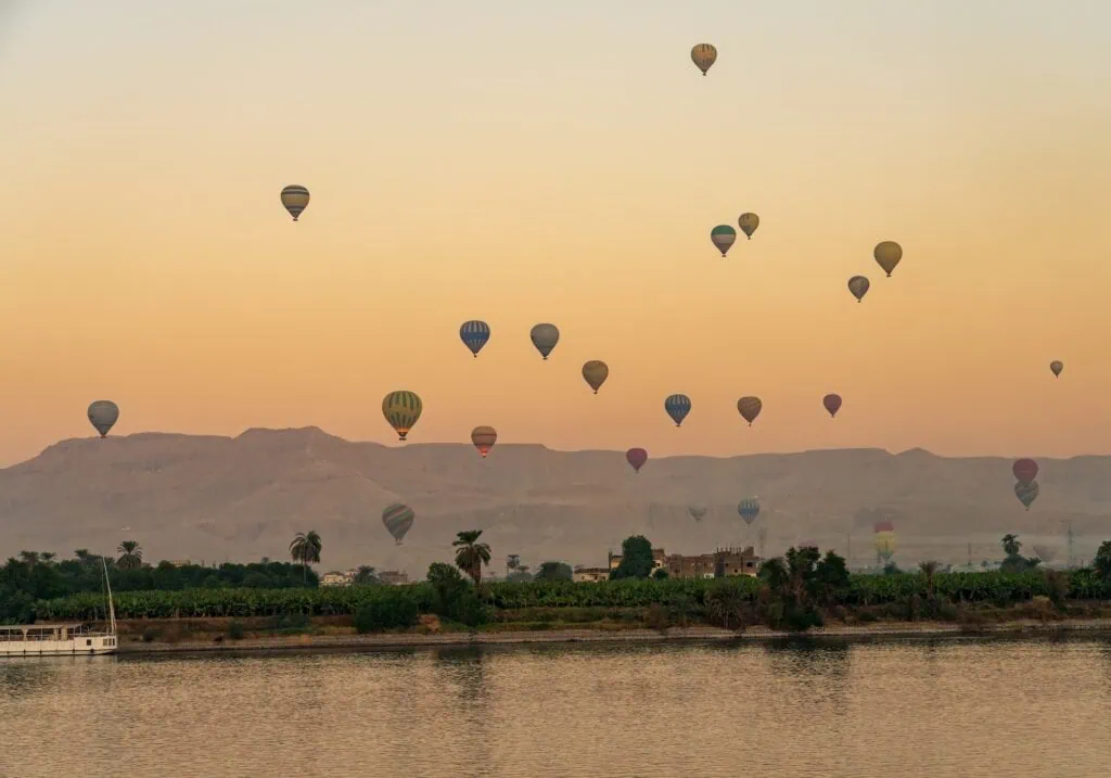 Multiple hot air balloons floating above the Nile River at sunset during flights over the Valley of the Kings