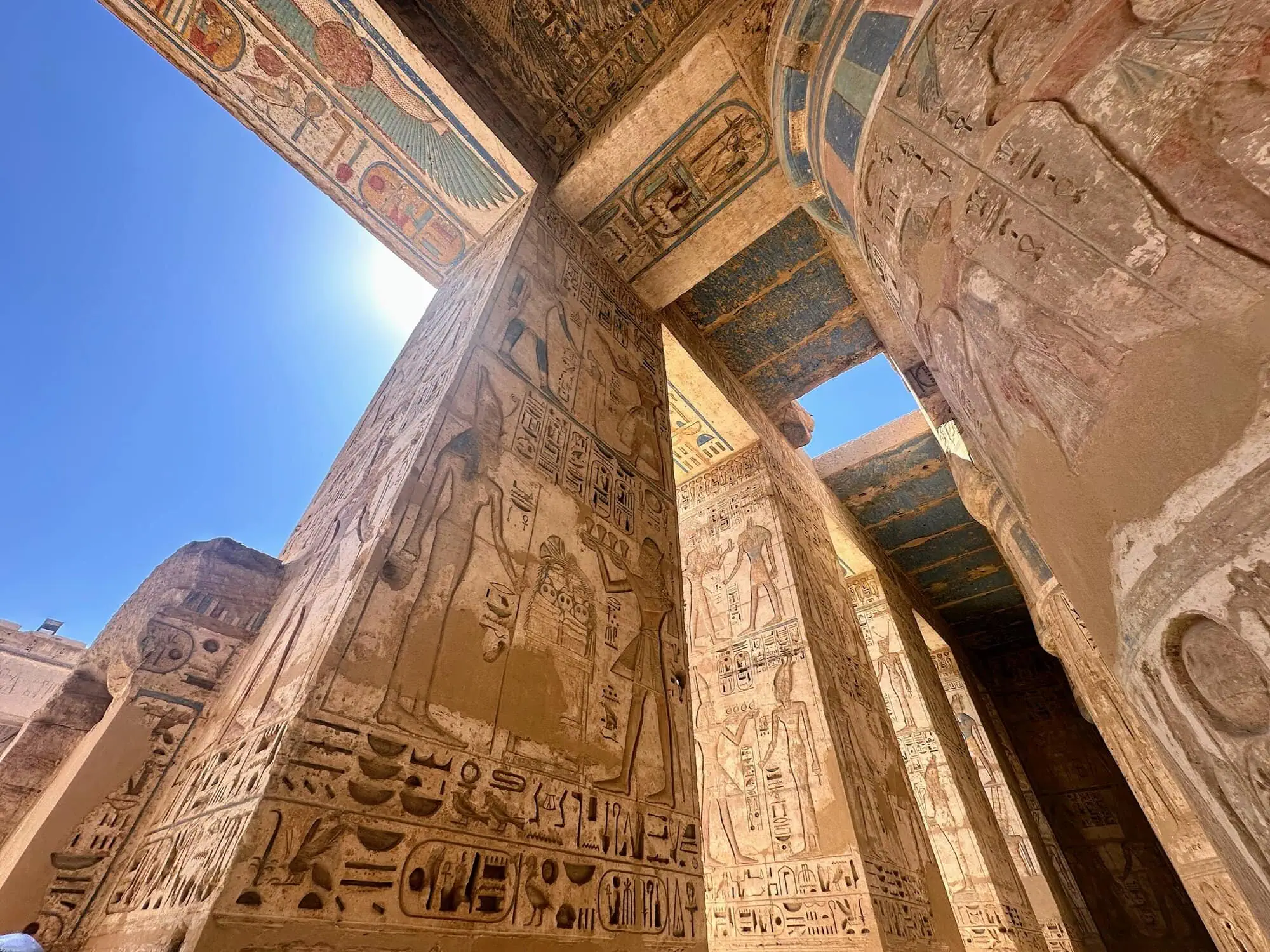 Interior of Medinet Habu temple showing massive columns with colorful hieroglyphic carvings and painted ceiling