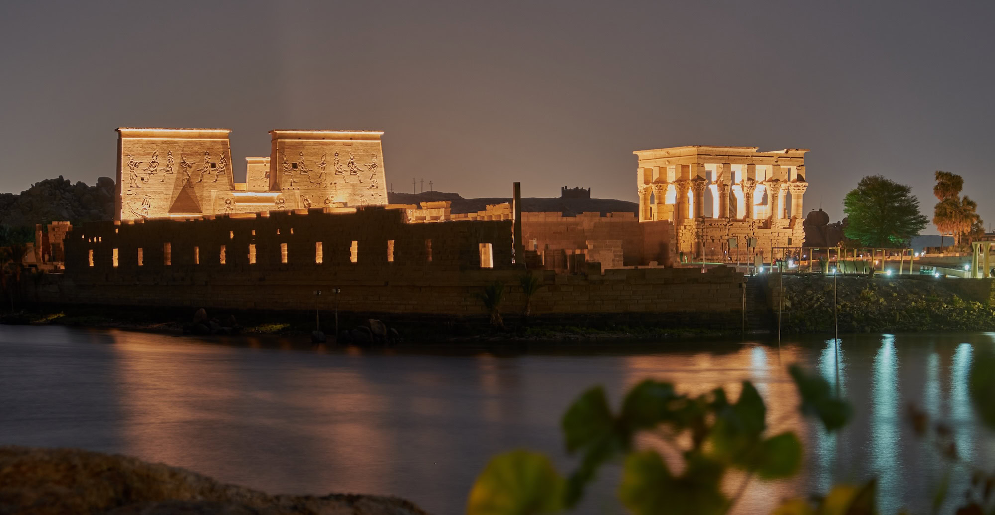 Ancient Philae Temple with illuminated columns and hieroglyphs reflected in the Nile River at Aswan