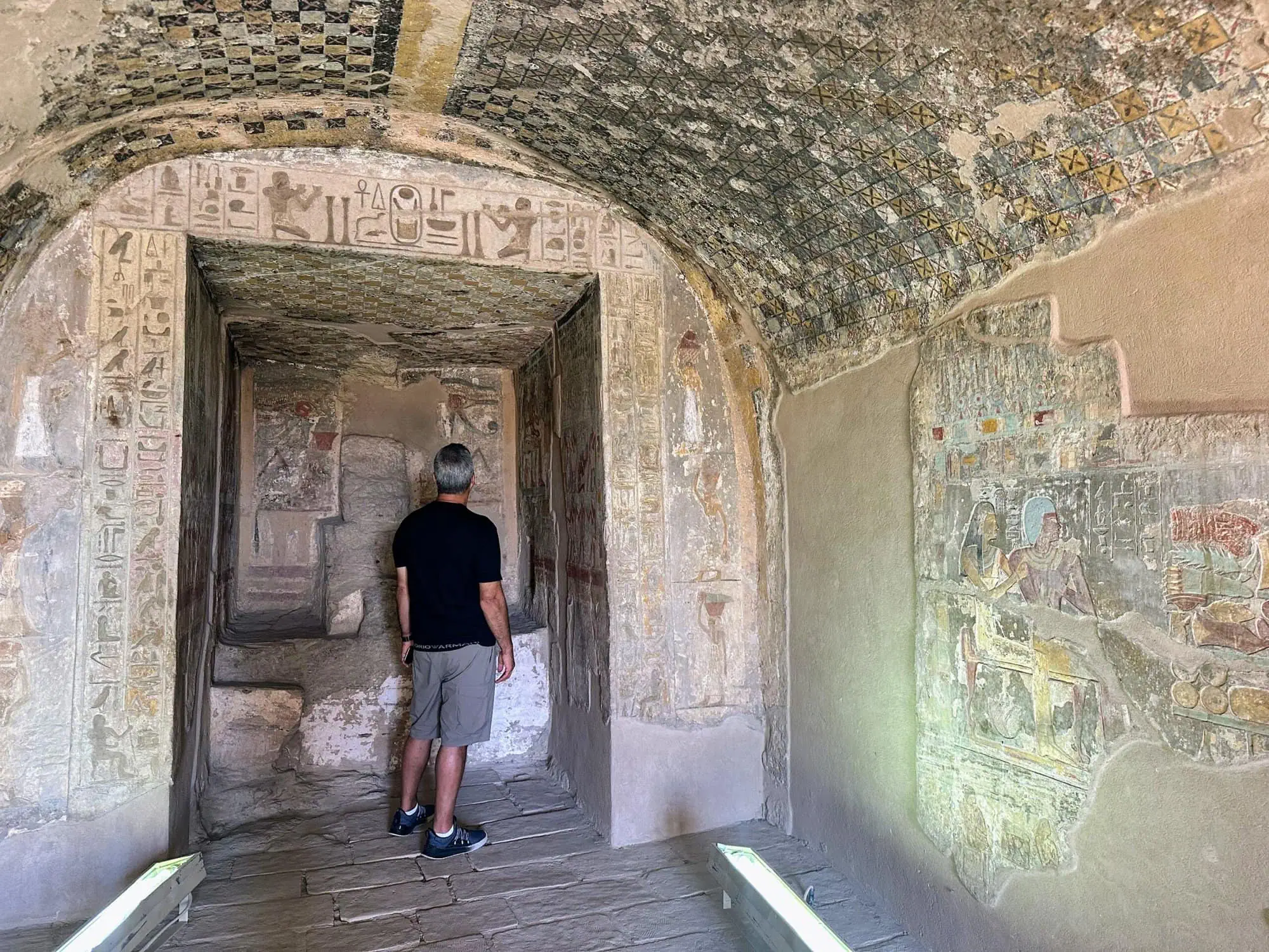 Tourist standing in ancient Egyptian tomb chamber with hieroglyphs and painted ceiling