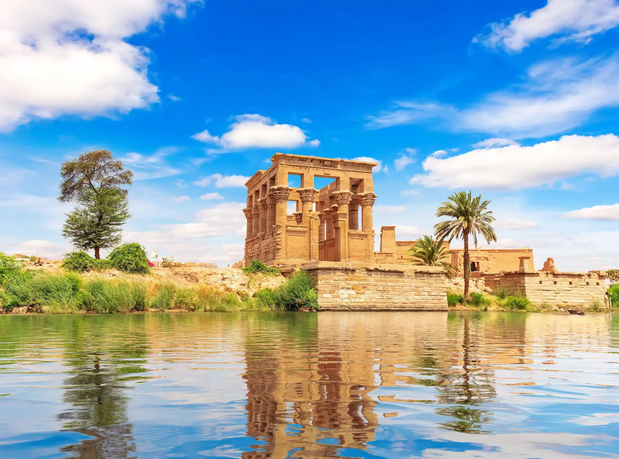 Philae Temple reflected in peaceful waters with palm trees and ancient columns
