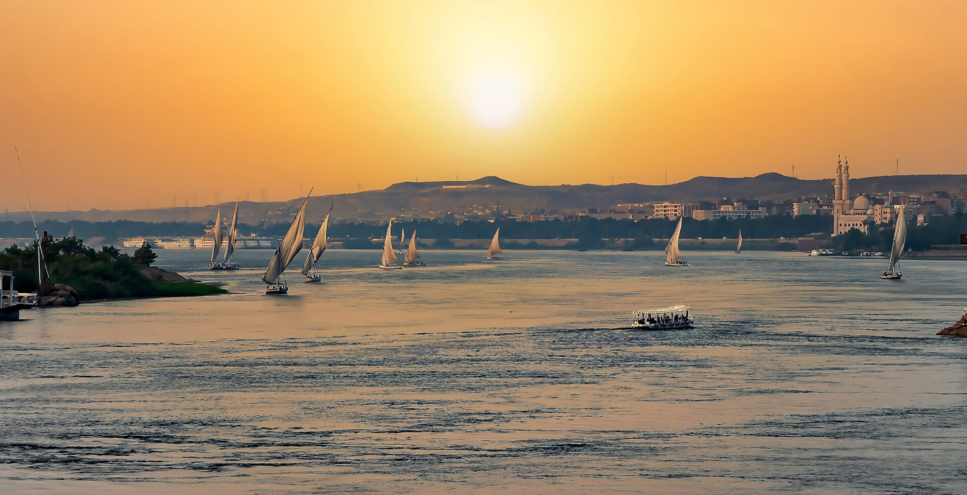 View of a beautiful orange sunset in Aswan Egypt with a lot of felucca sailing in the Nile river 1905x976 crop 49 61