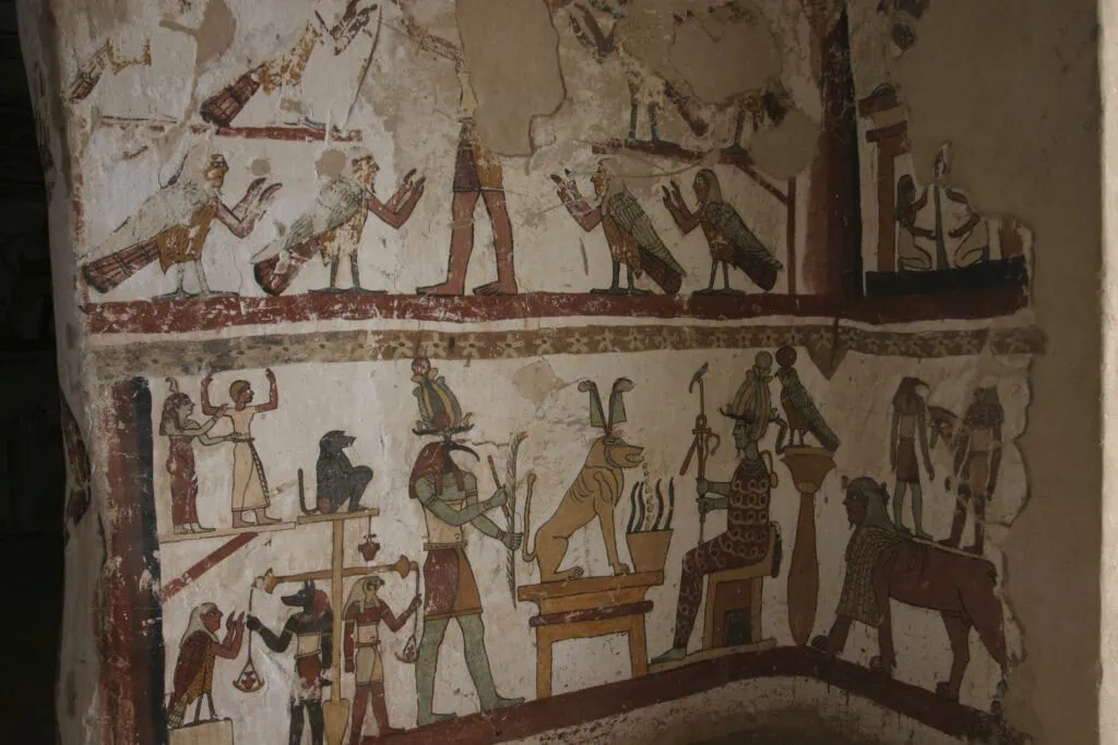 Painted wall reliefs inside the Tomb of Petosiris at Tuna el-Gebel, showing figures with the proportions and clothing of Greek classical art carrying out traditional Egyptian religious scenes, with hieroglyphic inscriptions surrounding them.