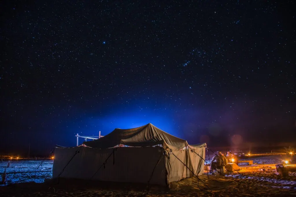 Desert camp with tents and seating illuminated beneath a clear star-filled night sky in the Sinai Desert, Nuweiba