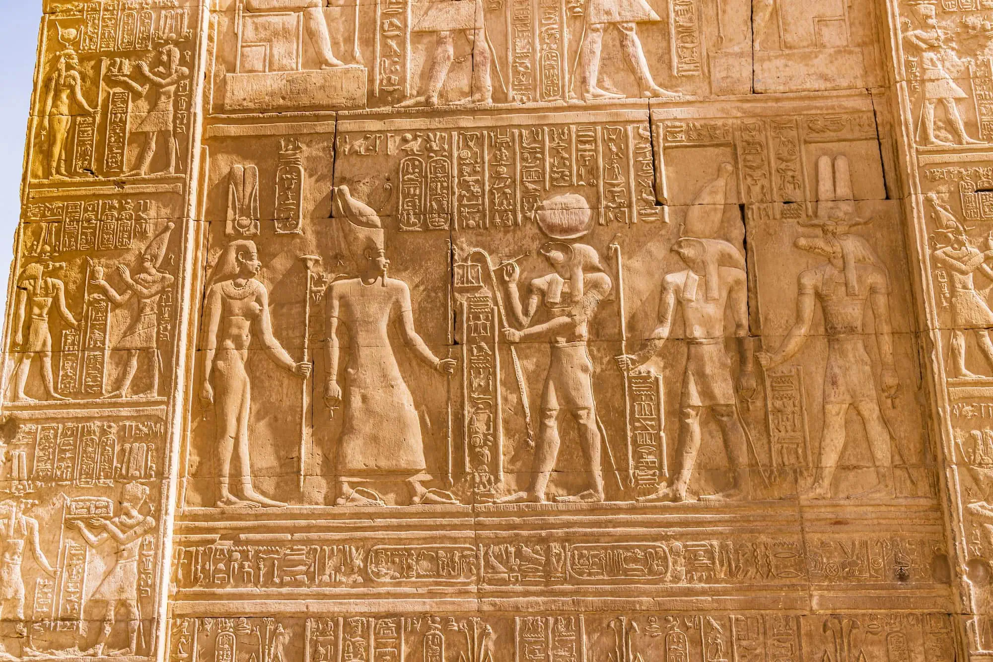 Jeroglíficos egipcios antiguos tallados en pared de templo con figuras de faraón y deidades