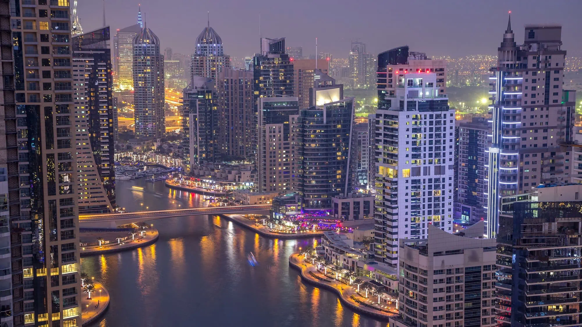 Illuminated Dubai Marina skyscrapers and boats at dusk