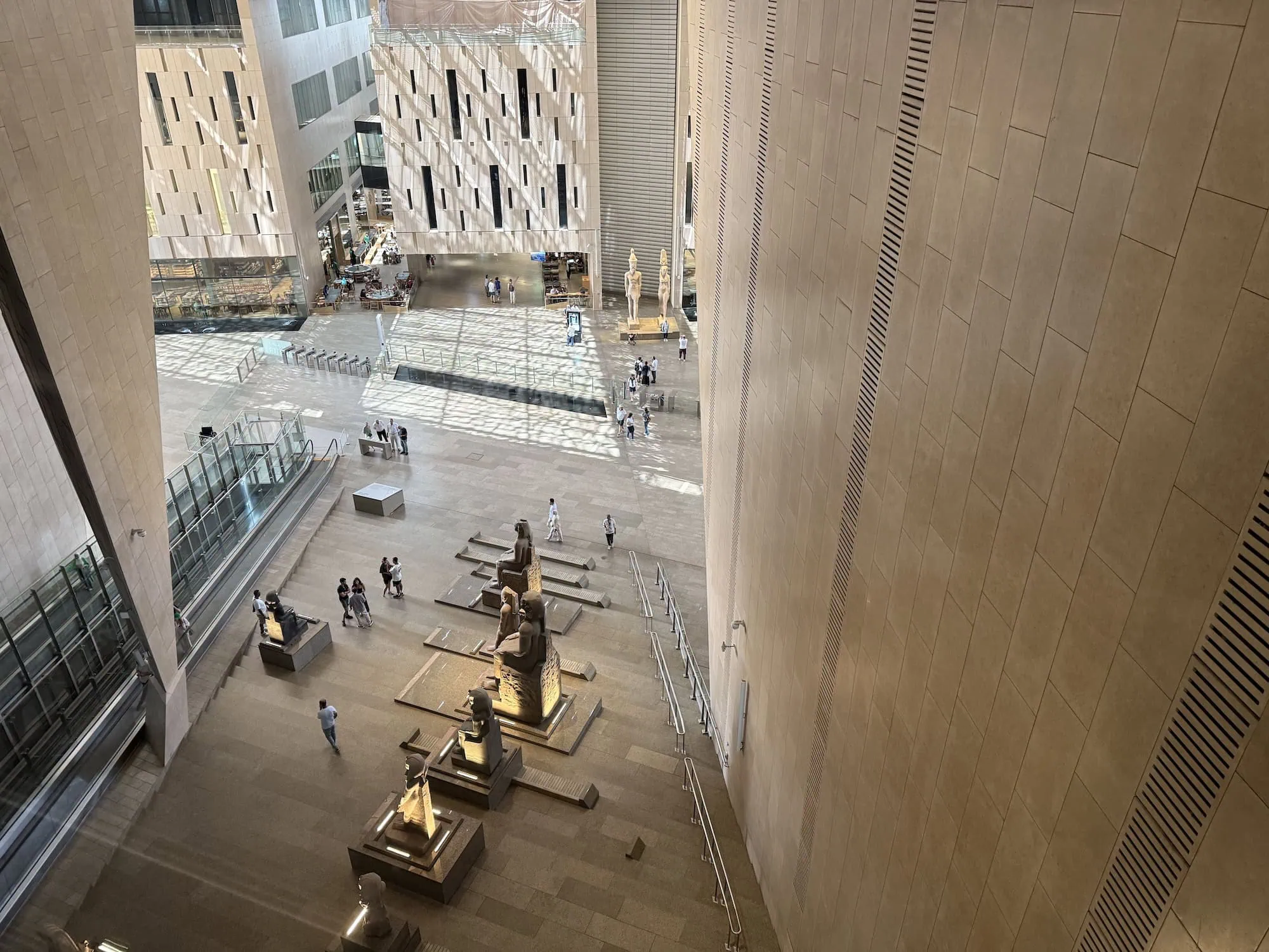 Interior of Grand Egyptian Museum showing ancient Egyptian statues and artifacts with visitors exploring the exhibition space
