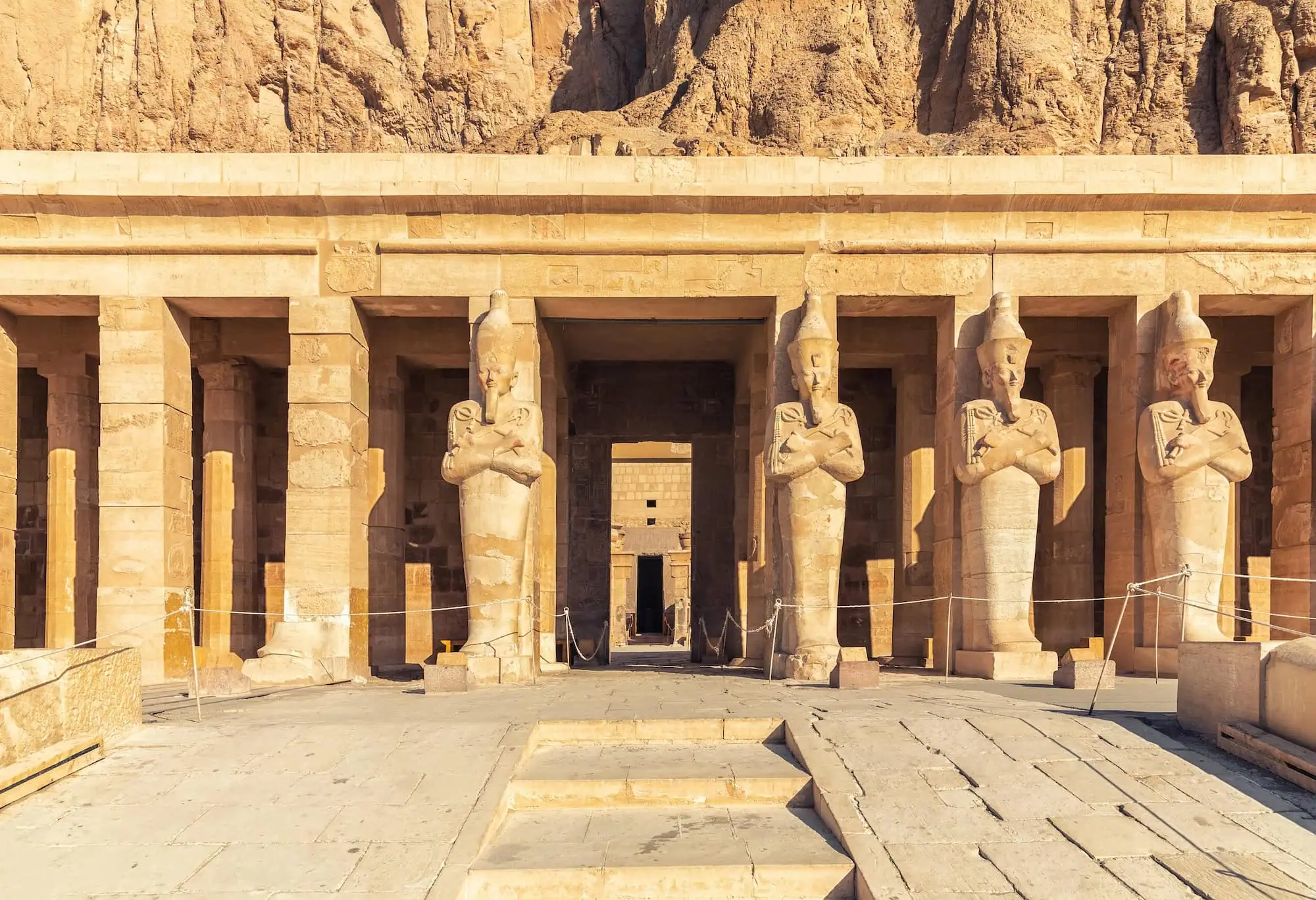 Ancient pharaoh statues at the Mortuary Temple of Hatshepsut against limestone cliffs in Egypt