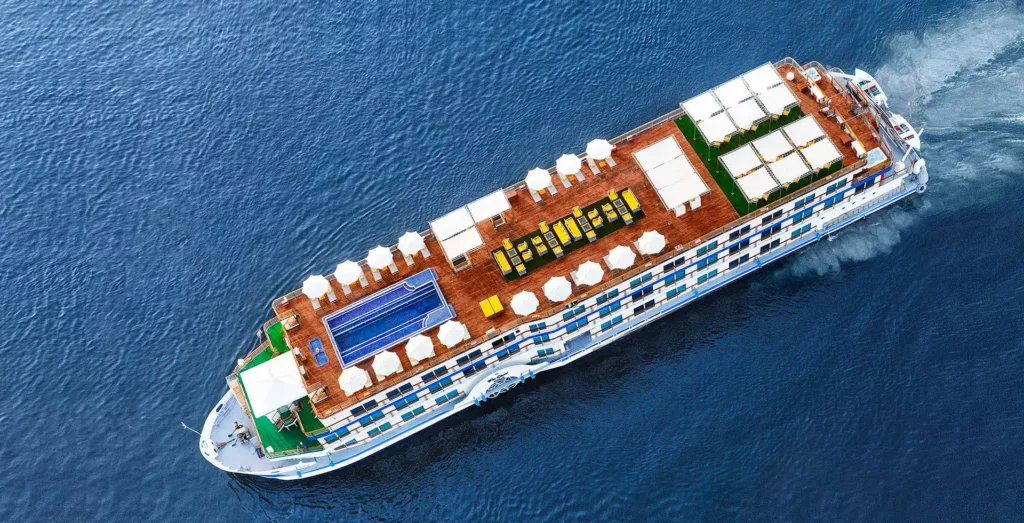An aerial view of the sun deck and swimming pool aboard a 5-star Nile cruise vessel, with rows of sun loungers, shaded seating areas, and the Nile visible on both sides.