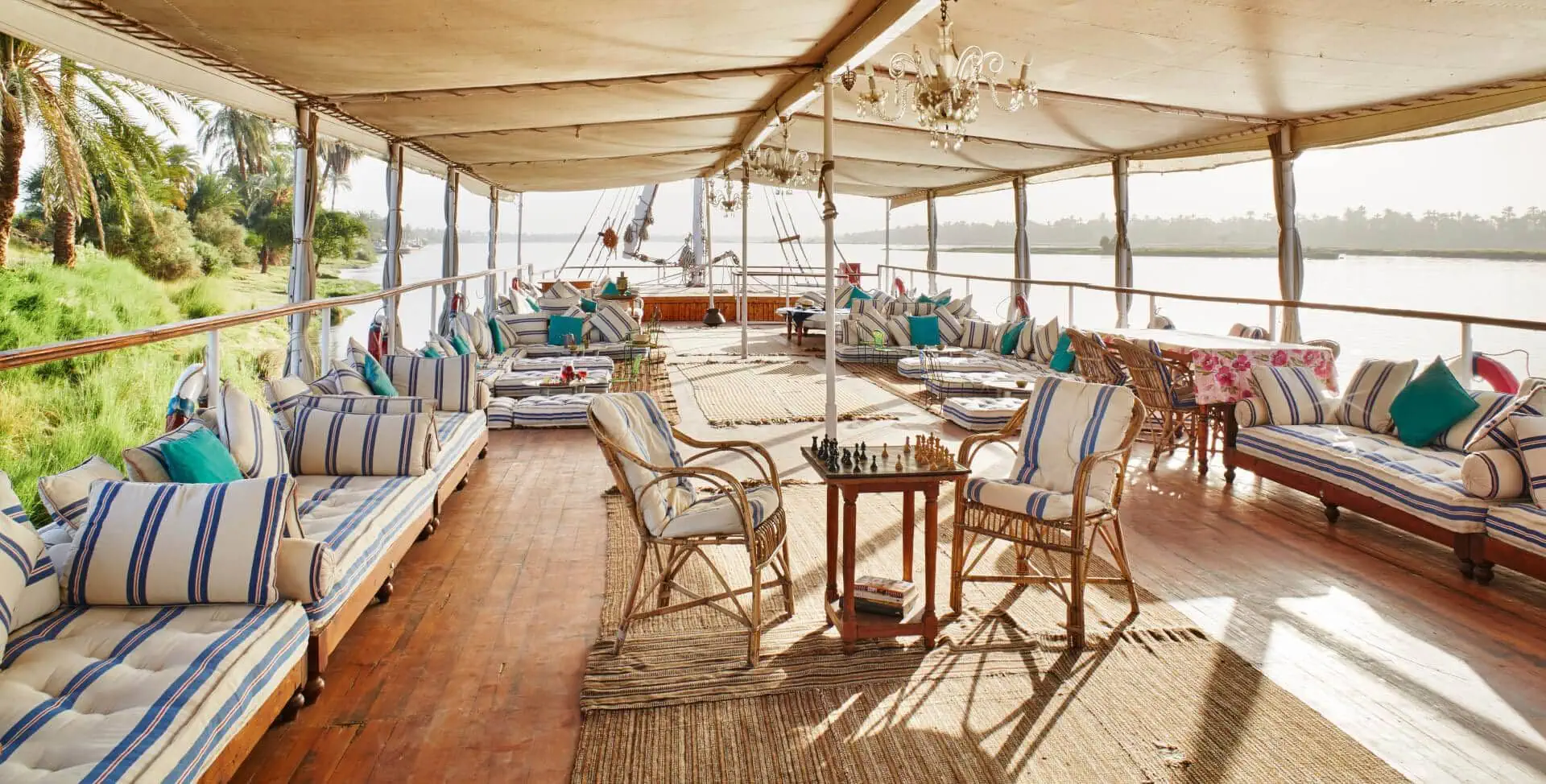 The lounge deck of a traditional dahabiya sailing vessel on the Nile, furnished with a chandelier, a chess set, and comfortable seating.