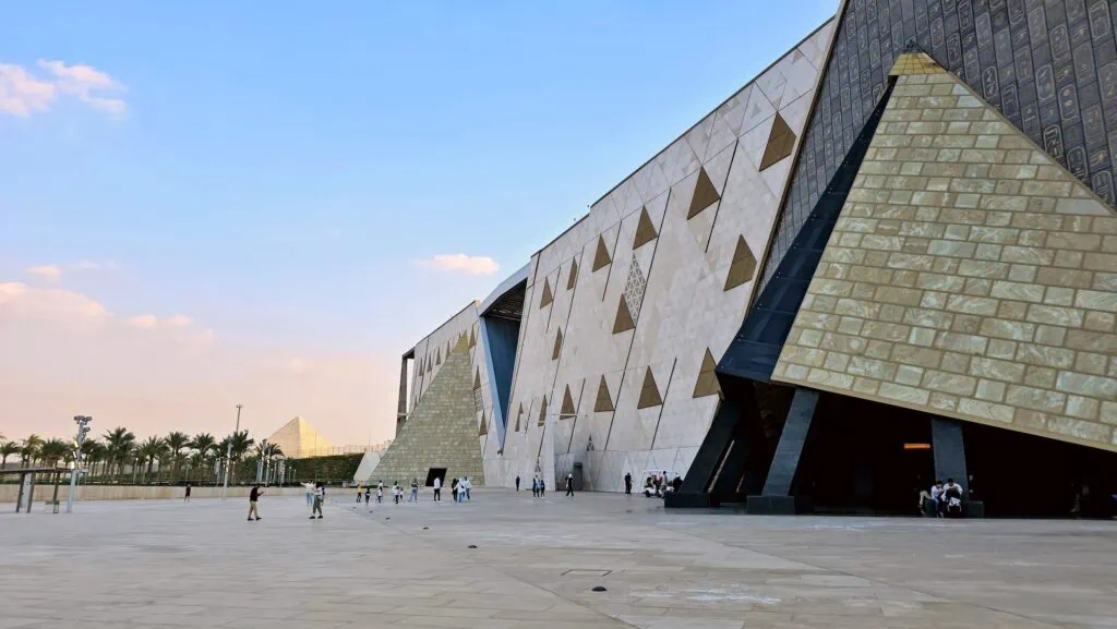 Entrance facade of the Grand Egyptian Museum at Giza, fully open since 2025, housing more than 100,000 pharaonic artefacts including the complete Tutankhamun collection of 5,000+ items displayed together for the first time since the king's burial in 1323 BC.