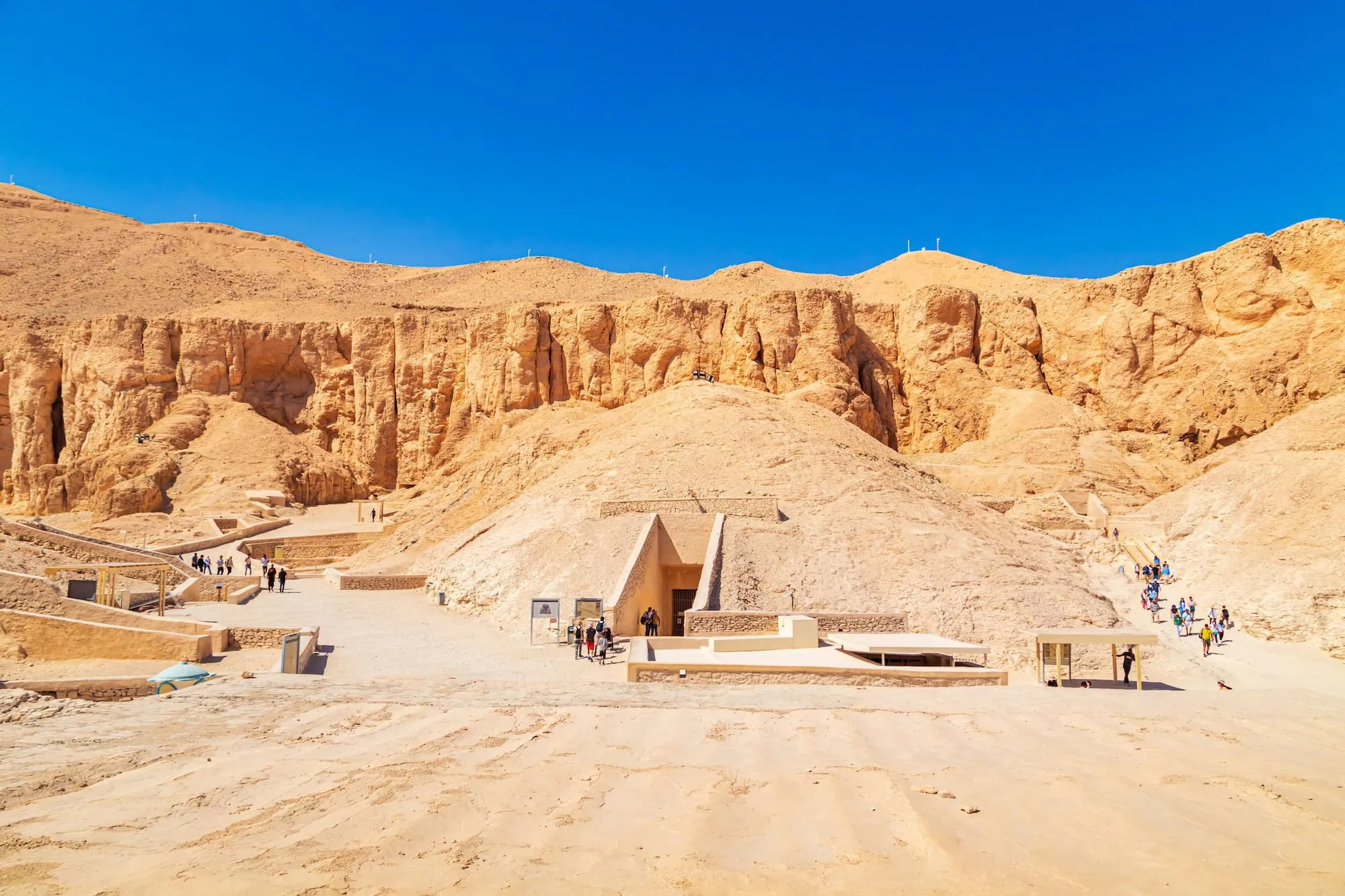 Tourists walking along pathways near ancient tomb entrances in Valley of the Kings