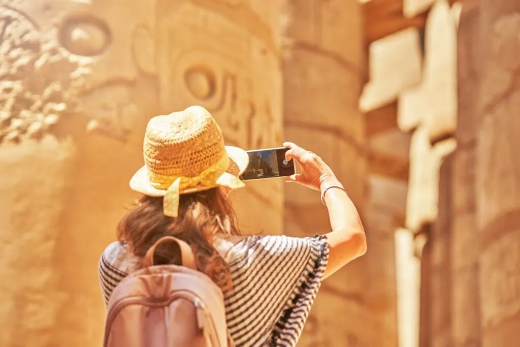 A woman photographing the towering ancient columns of the Karnak Temple in Luxor, Egypt.
