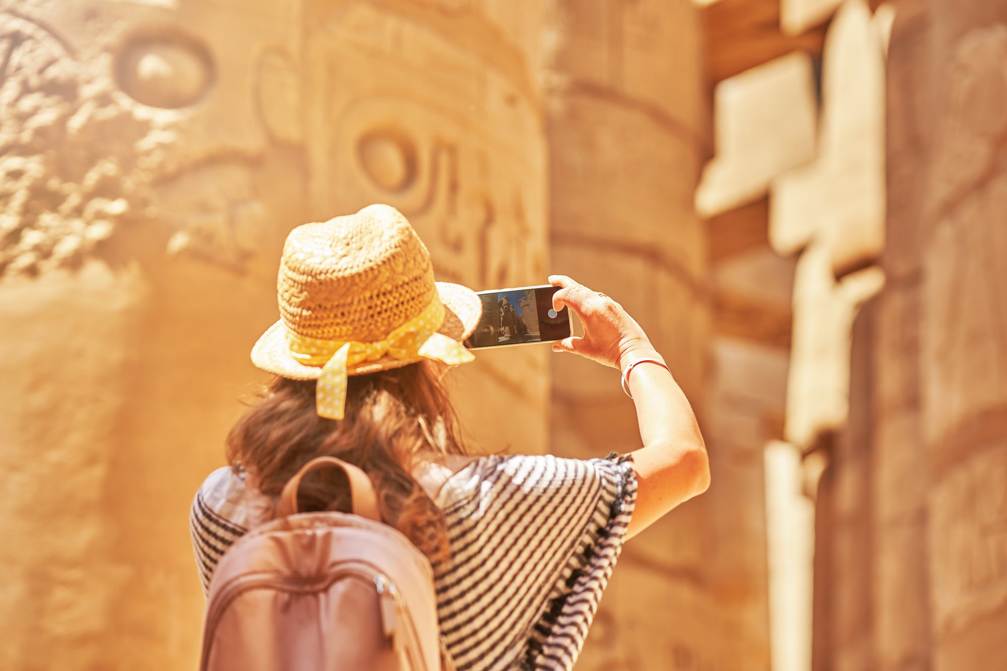 Tourist with backpack exploring ancient Egyptian temple with hieroglyphs and stone columns