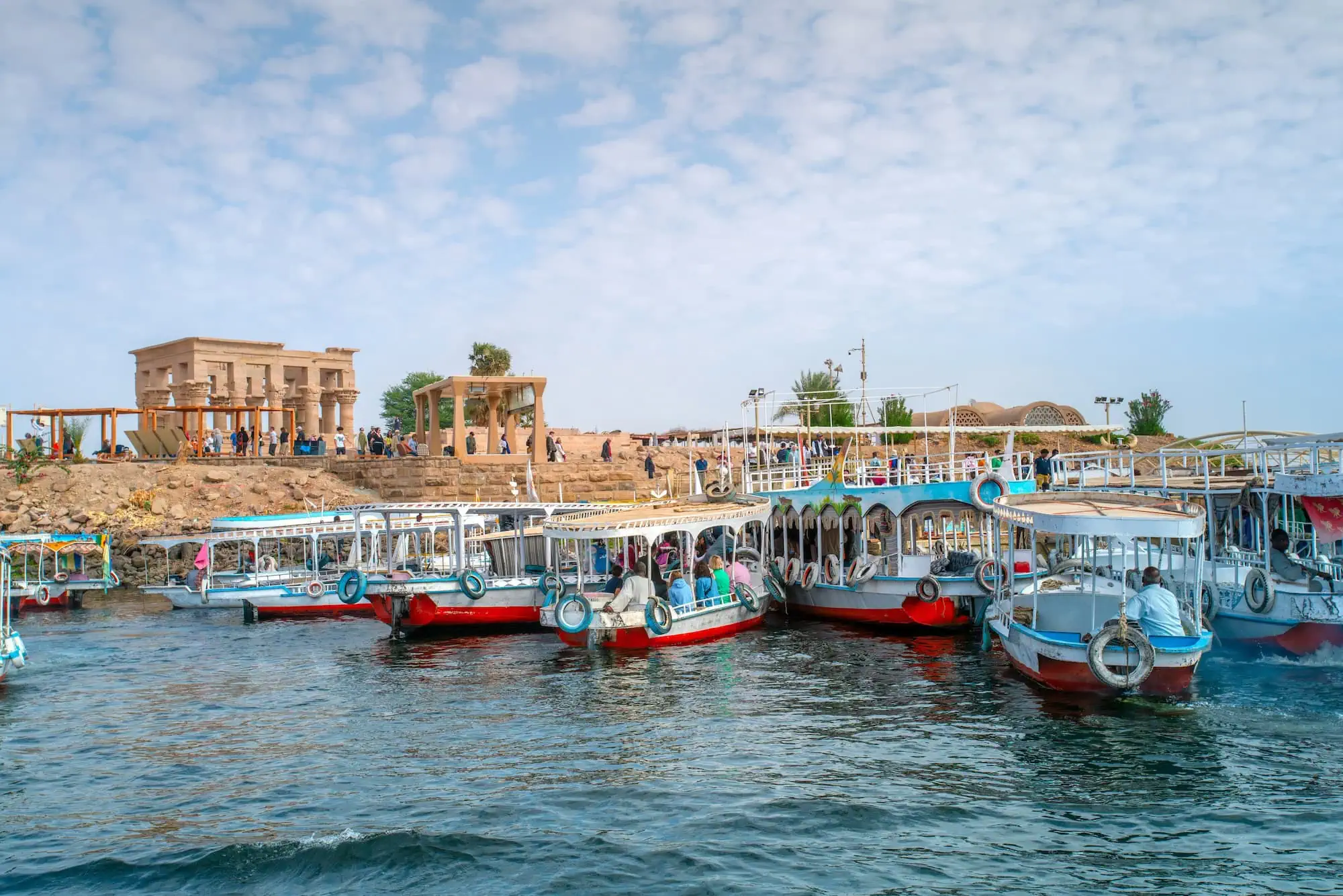 Tourist boats docked at the ancient Philae Temple in Aswan with stone columns and Nile River waters