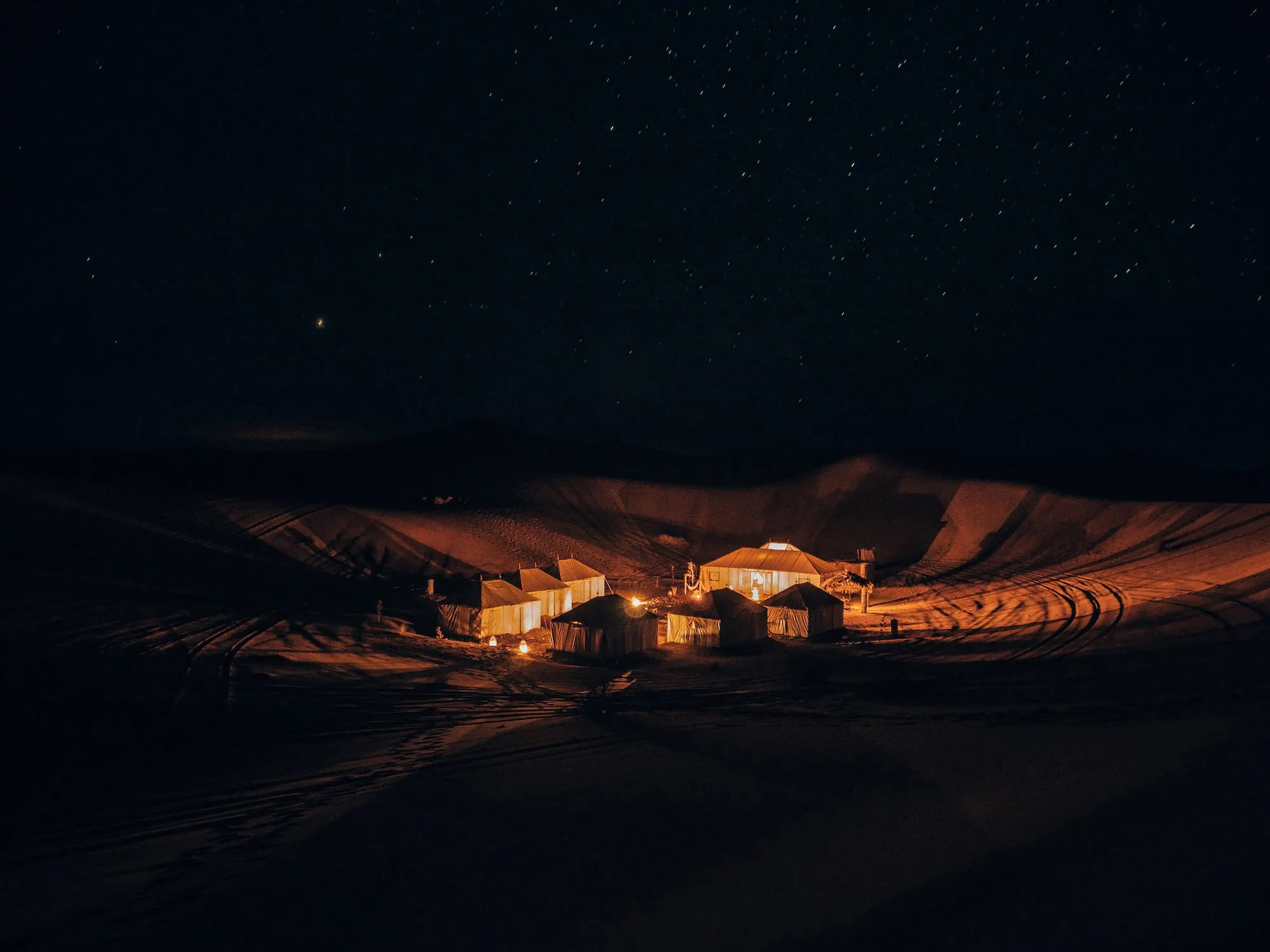 Desert camping tents under a starry night sky with campfire lights