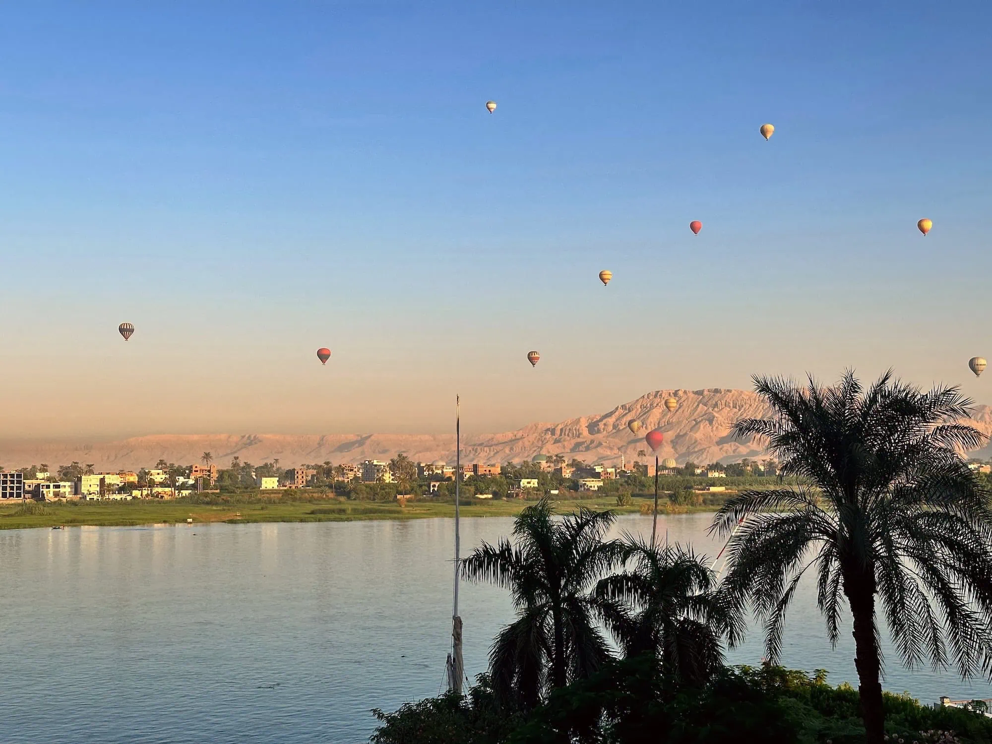 Hot air balloons floating over the Nile River at Luxor, Egypt with desert mountains in background