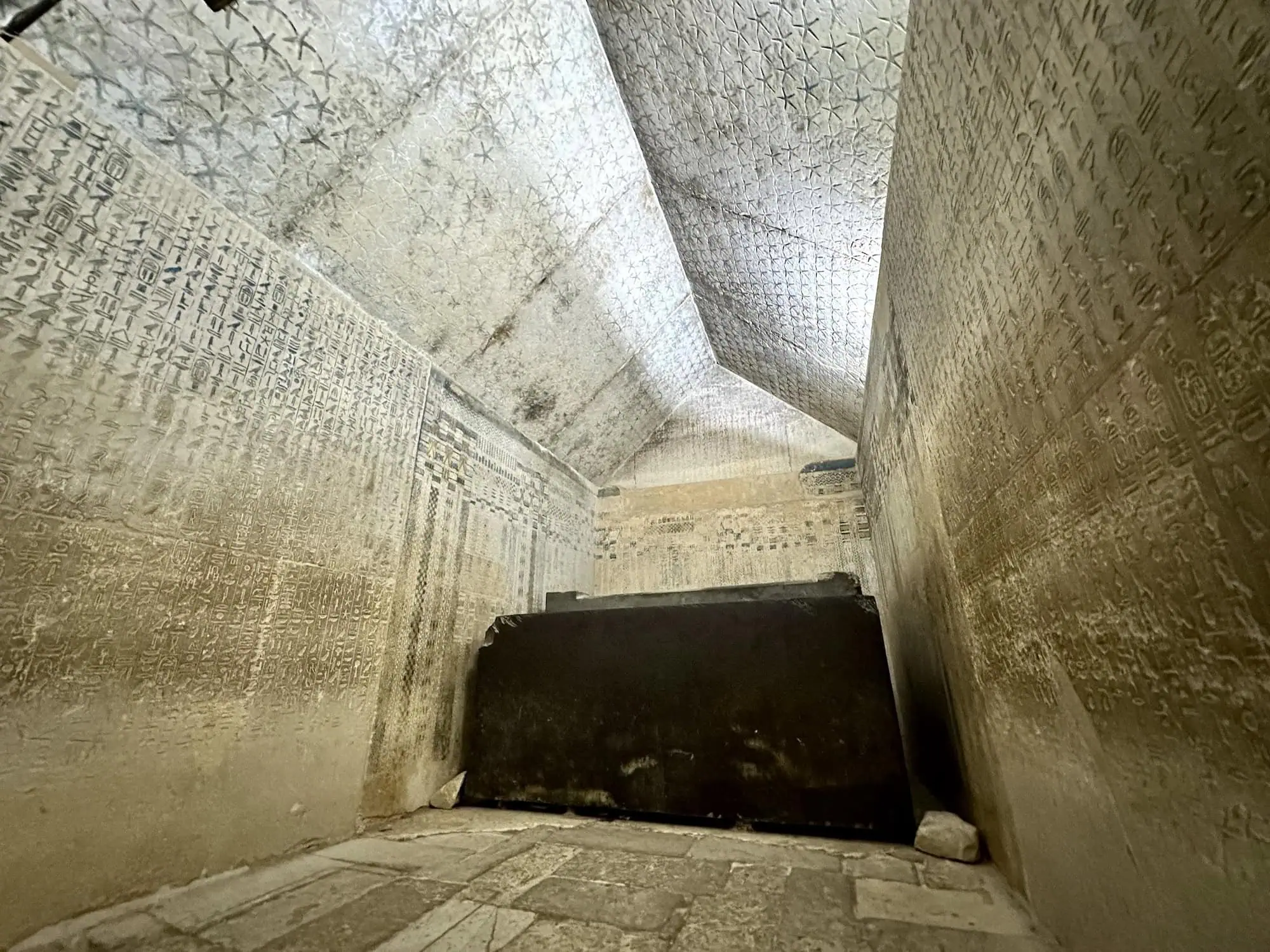 Burial chamber inside the Pyramid of Unas at Saqqara, with hieroglyphic Pyramid Texts covering the limestone walls and the granite sarcophagus visible at the centre