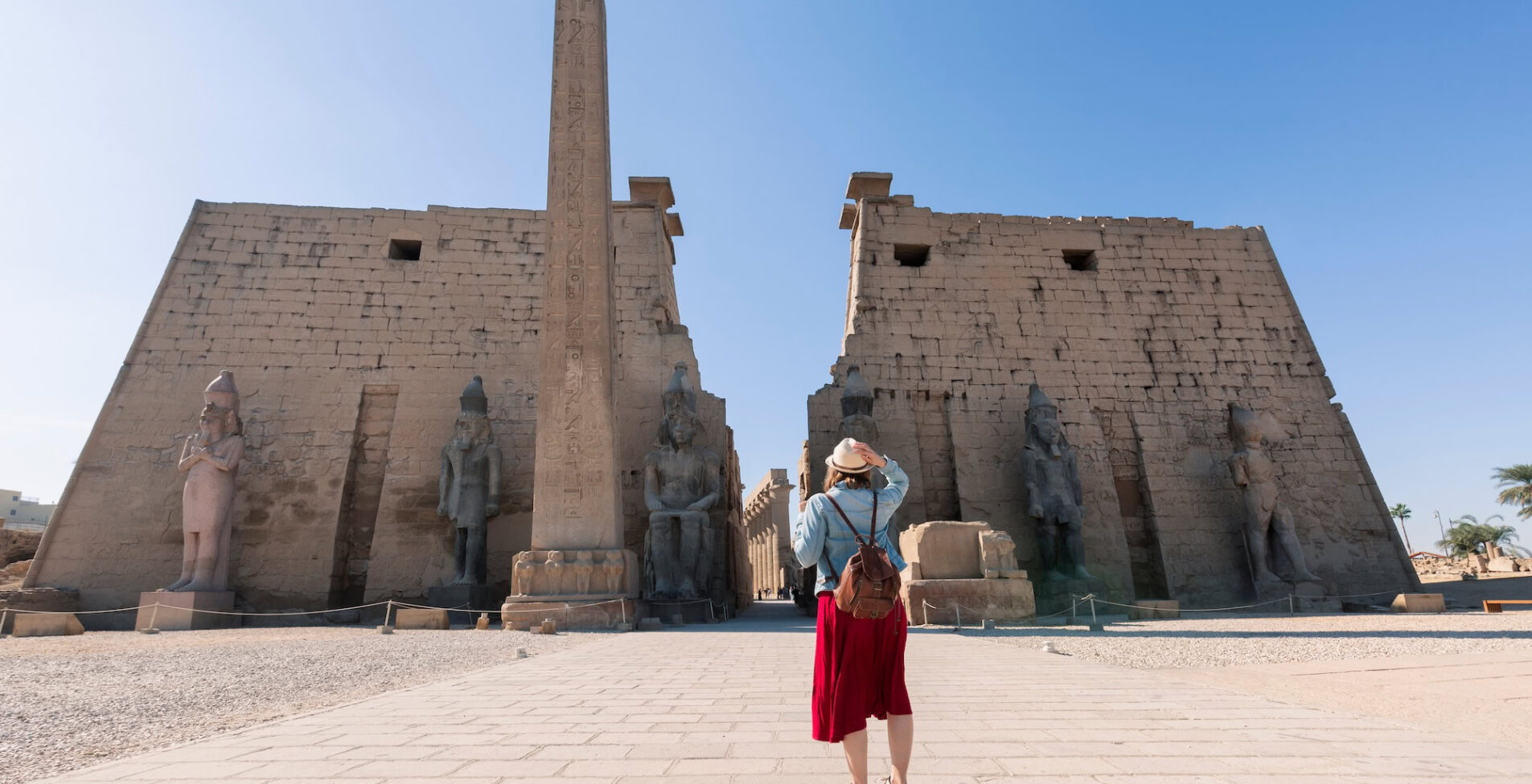 A blonde woman with a straw hat looks at the entrance to the Luxor Temple in Luxor LP