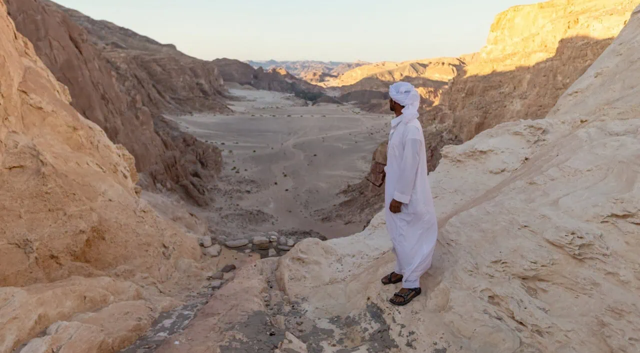 Bedouin man wearing traditional white clothes looking at the desert valley in South Sinai, Egypt