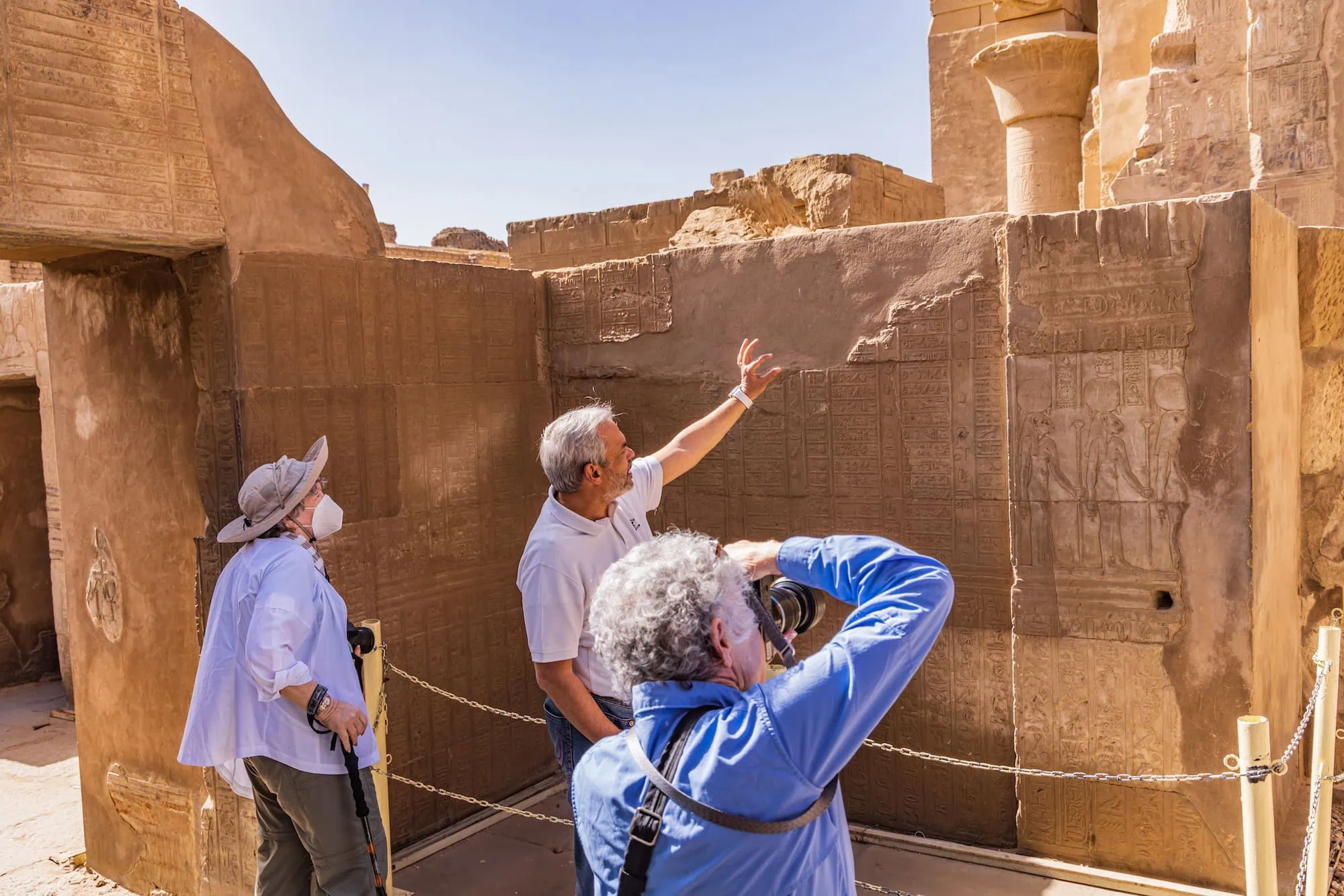 A private Egyptologist guide standing in front of carved hieroglyphic reliefs at Kom Ombo Temple, explaining the imagery to travelers