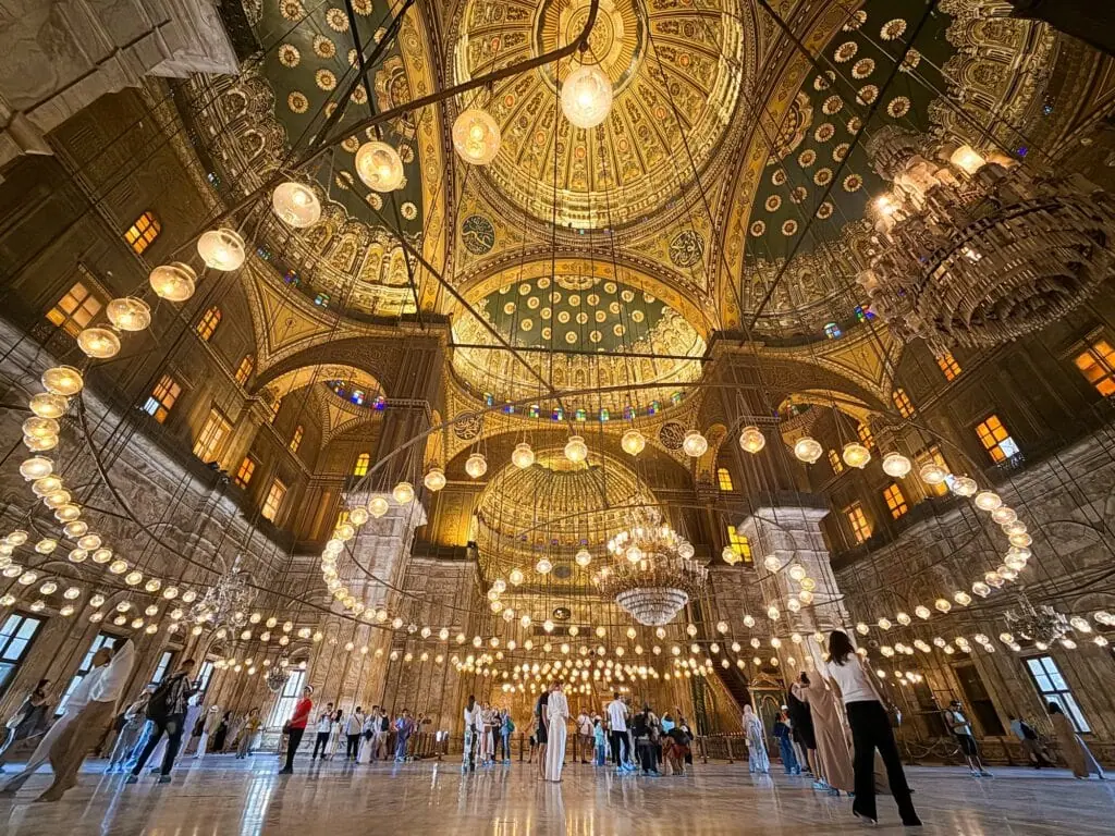 Interior view of the Mosque of Muhammad Ali inside the Citadel of Cairo, Egypt — domed Ottoman-style prayer hall with chandeliers and visitors, built between 1830 and 1848