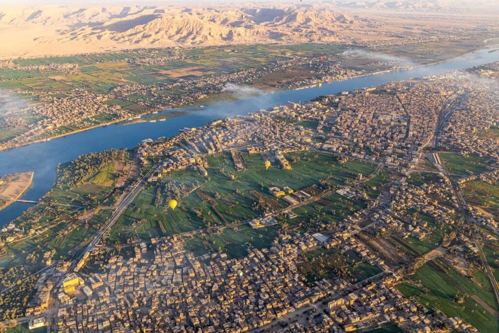 Panoramic view of the Nile River, city buildings, and surrounding farmland seen from a hot air balloon over Luxor