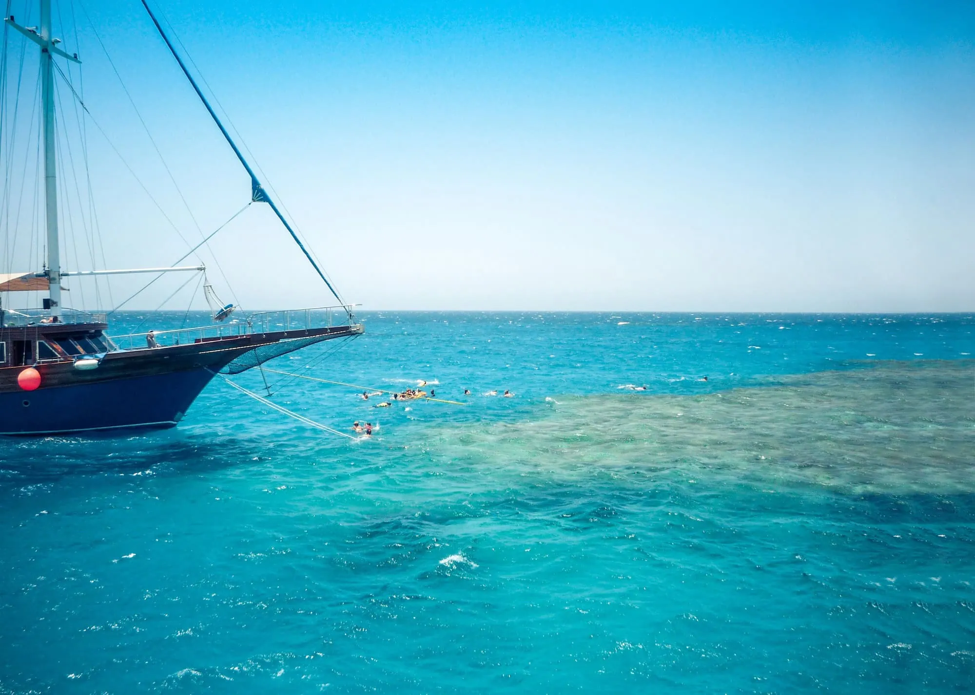 Tourists snorkeling and swimming near a sailboat in the crystal clear turquoise waters of Ras Mohamed National Park