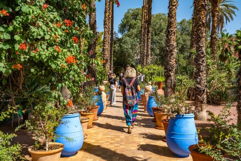 A view from the popular landmark Majorelle Garden, showing tourists walking between palm treesn and blue and brown flowerpot