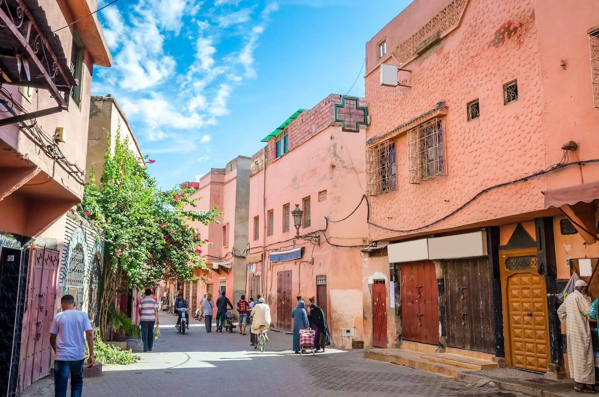 Bustling street scene in Marrakesh's old medina with traditional pink buildings and local residents