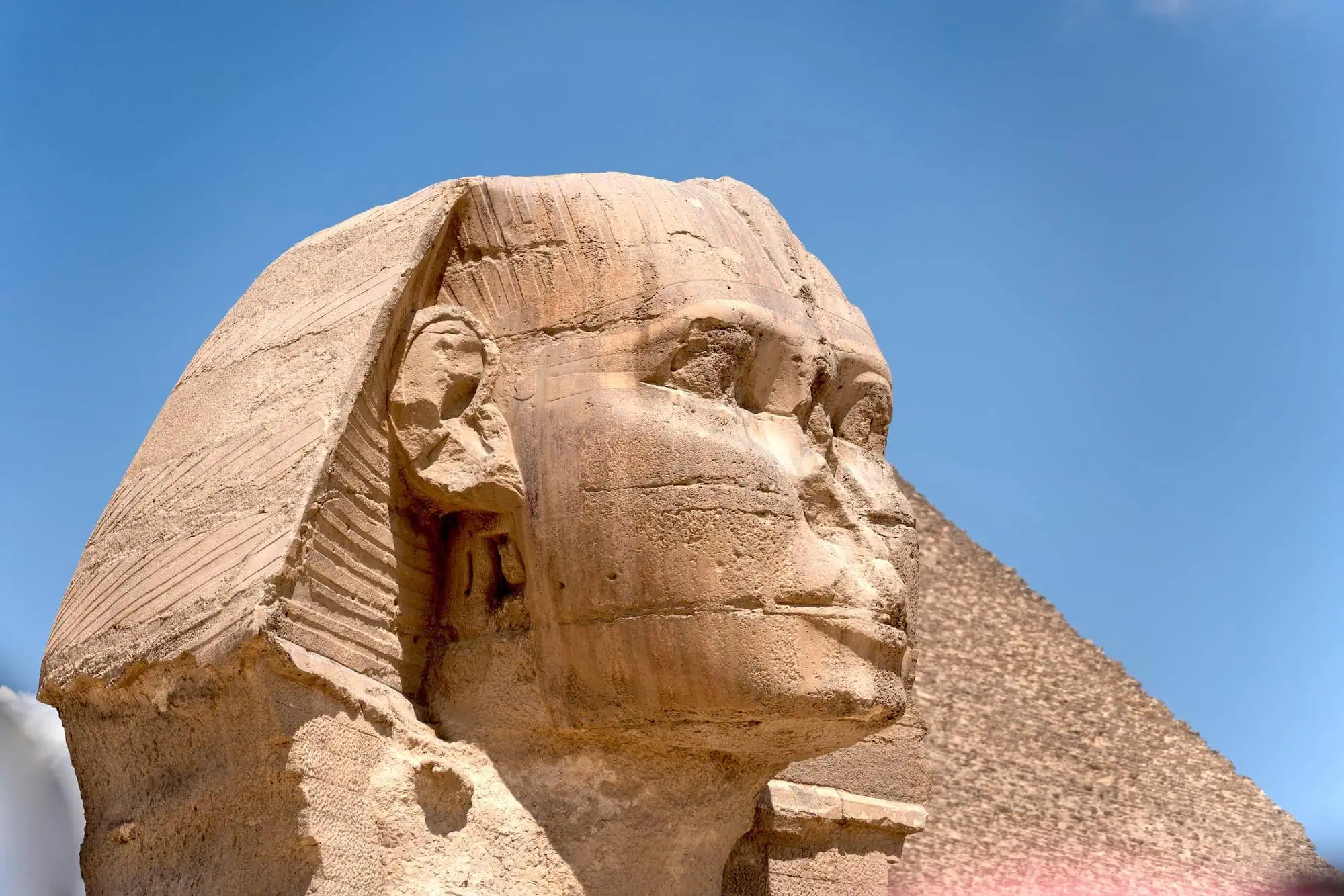 Close-up of the weathered limestone head of the Great Sphinx of Giza, carved from a single bedrock ridge beside the pyramid of Khafre.