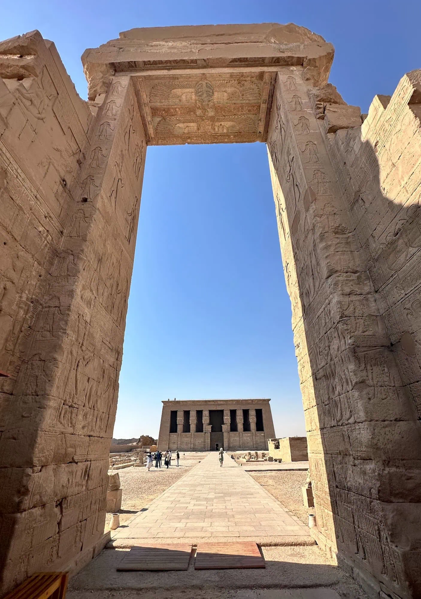 The ancient stone gateway and Hathor-headed columns of the Temple of Hathor at Dendera, covered in hieroglyphic carvings, photographed under clear sky north of Luxor.