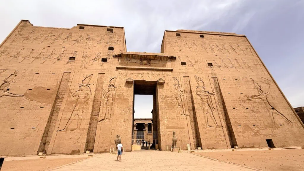 The massive pylon entrance of the Temple of Horus at Edfu, Egypt — a Ptolemaic-era temple built between 237 and 57 BC, with carved reliefs of Ptolemy XII smiting his enemies