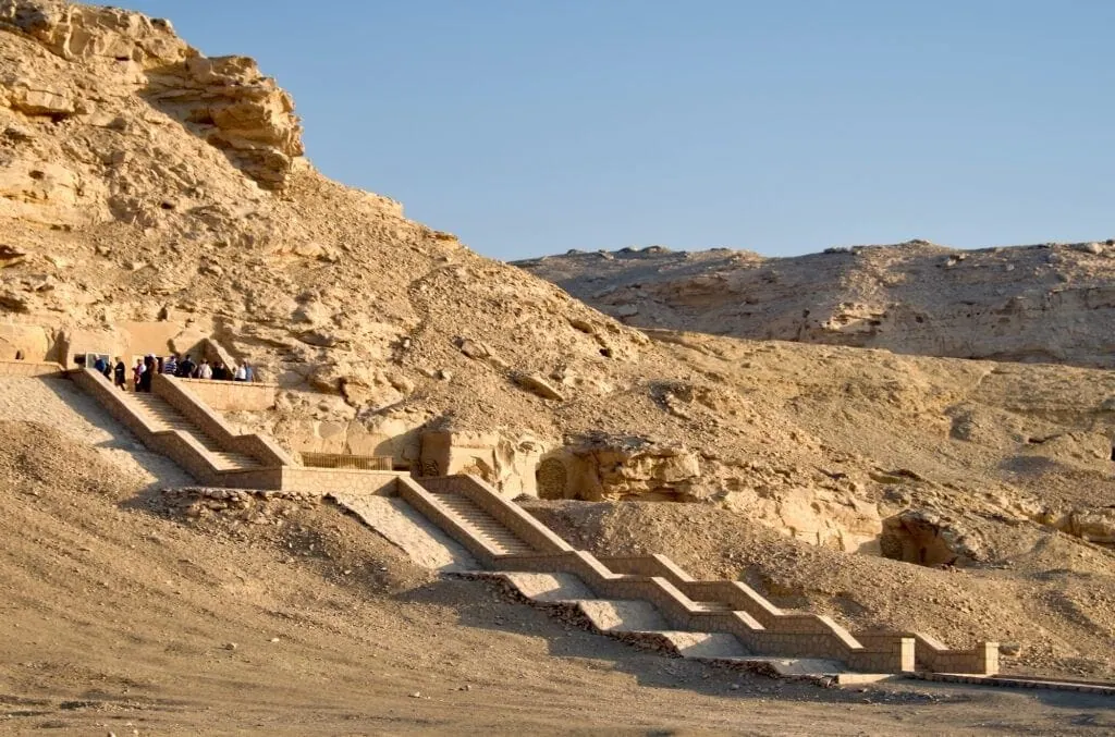The cliff-face rock-cut tombs of the Nekheb necropolis at El-Kab on the east bank of the Nile, photographed at dawn with the desert plateau and 18th-dynasty tomb entrances visible.