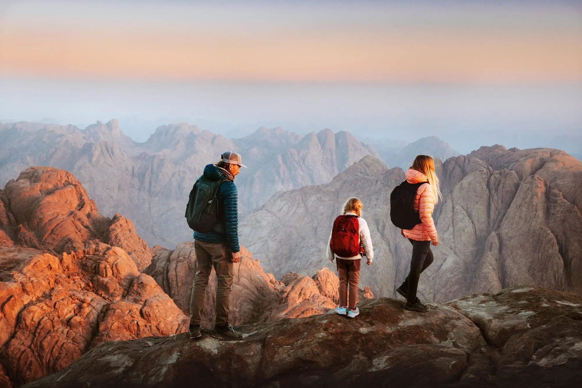 Family of hikers enjoying sunrise view at Mount Sinai with dramatic mountain landscape