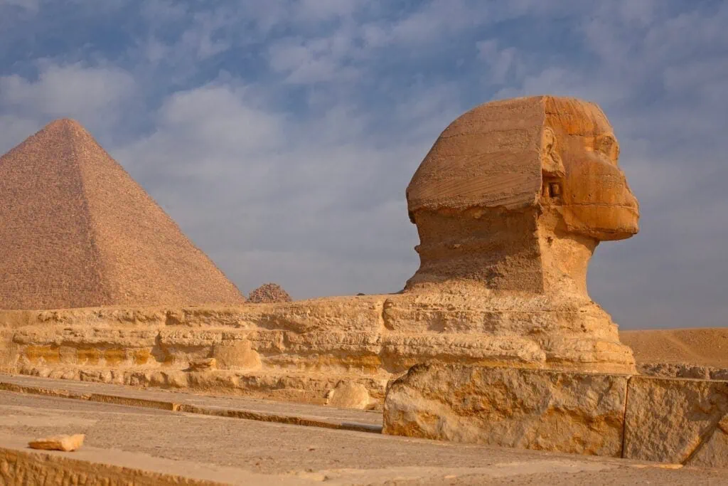 The Great Sphinx of Giza in the foreground with the Great Pyramid of Khufu rising behind on the desert plateau on the western edge of Cairo, photographed in clear morning light.