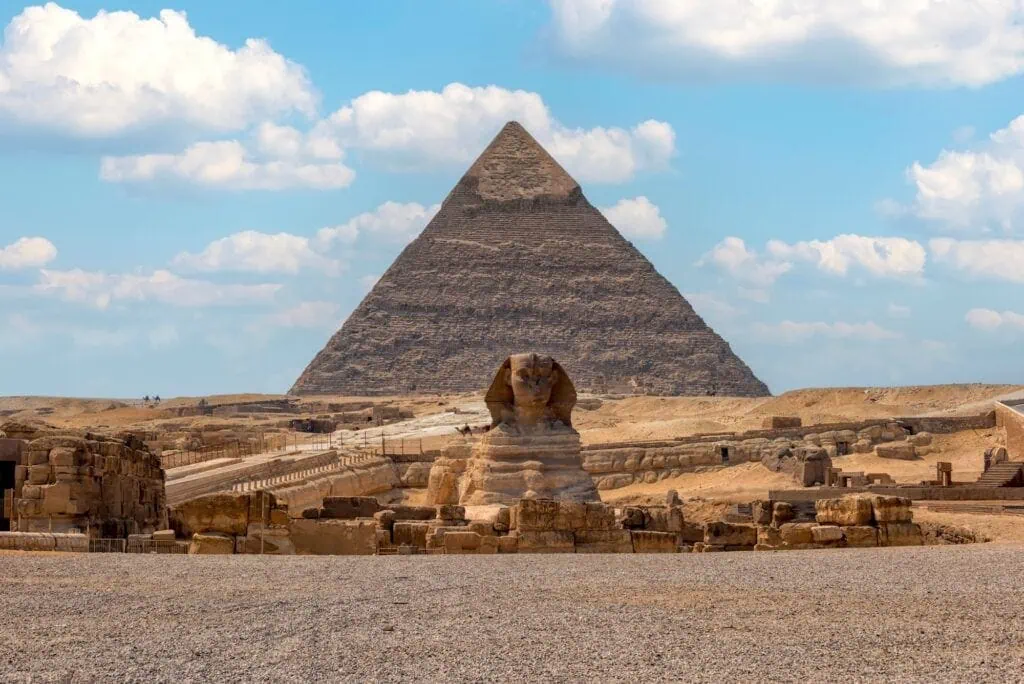 The Great Sphinx of Giza in the foreground with the pyramids rising behind it on the desert plateau at the edge of Cairo, Egypt.