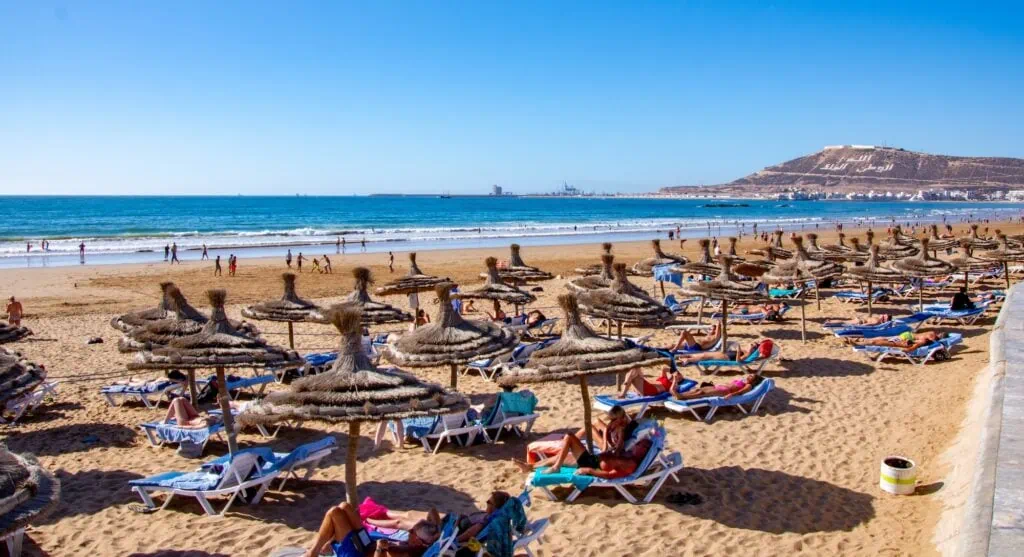 Sunny shoreline with ocean waves and beachfront promenade at Agadir Beach, Agadir
